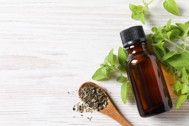 Essential oil in bottle, dry herbs and oregano leaves on white wooden table, flat lay. Space for text