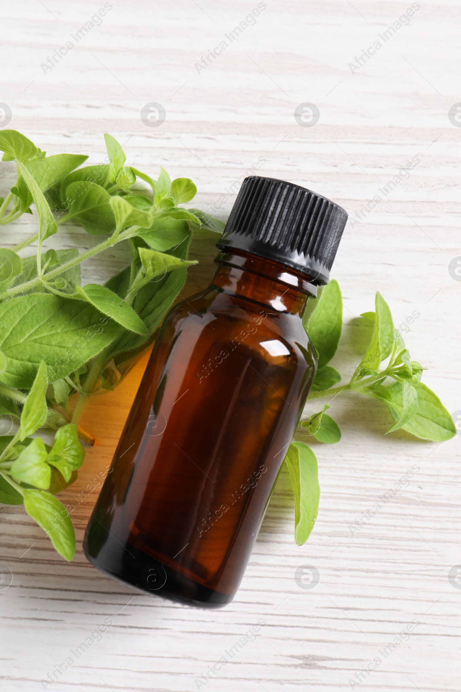 Photo of Essential oil in bottle and oregano leaves on white wooden table, top view