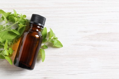 Essential oil in bottle and oregano leaves on white wooden table, top view. Space for text