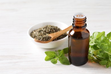 Essential oil in bottle, dry herb and oregano leaves on white wooden table, closeup. Space for text