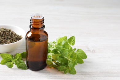 Essential oil in bottle, dry herb and oregano leaves on white wooden table, closeup. Space for text