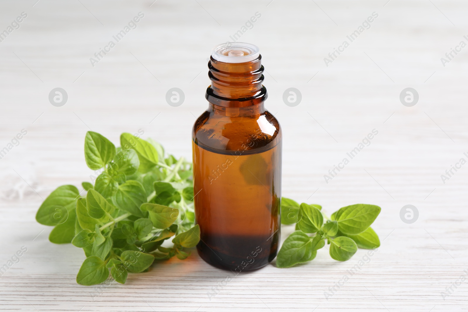 Photo of Essential oil in bottle and oregano leaves on white wooden table, closeup