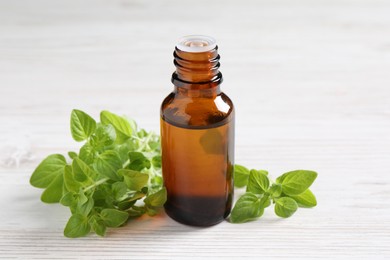 Essential oil in bottle and oregano leaves on white wooden table, closeup