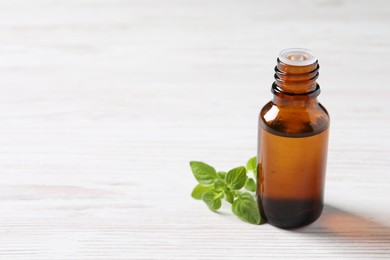 Essential oil in bottle and oregano leaves on white wooden table, closeup. Space for text