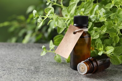 Essential oil in bottles, empty tag and oregano plant on grey textured table, closeup. Space for text