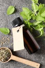 Essential oil in bottle with empty tag, dry herb and oregano leaves on grey textured table, flat lay