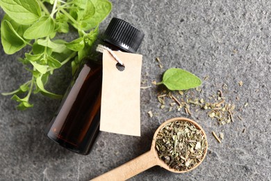 Essential oil in bottle with empty tag, dry herb and oregano leaves on grey textured table, flat lay