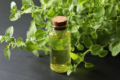 Essential oil in bottle and oregano twigs on dark textured table, closeup