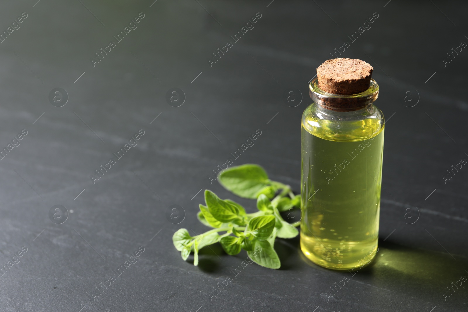 Photo of Essential oil in bottle and oregano twig on dark textured table, closeup. Space for text