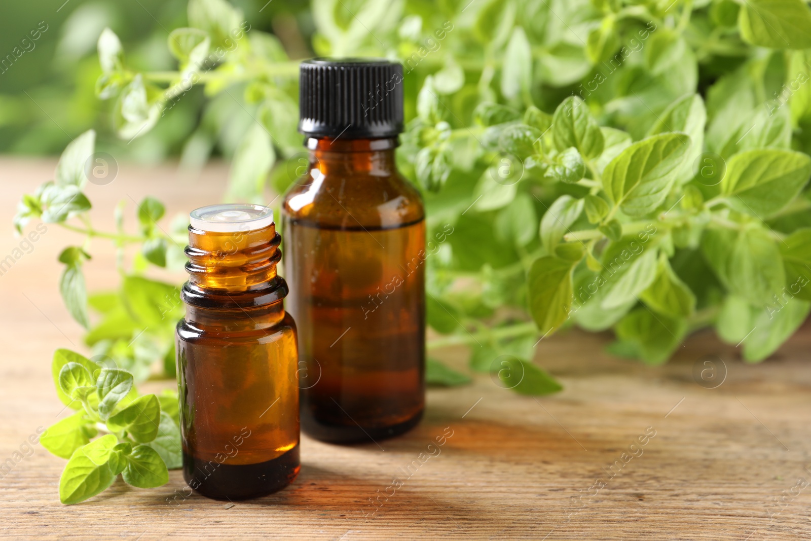 Photo of Essential oil in bottles and oregano twigs on wooden table, closeup