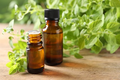 Essential oil in bottles and oregano twigs on wooden table, closeup