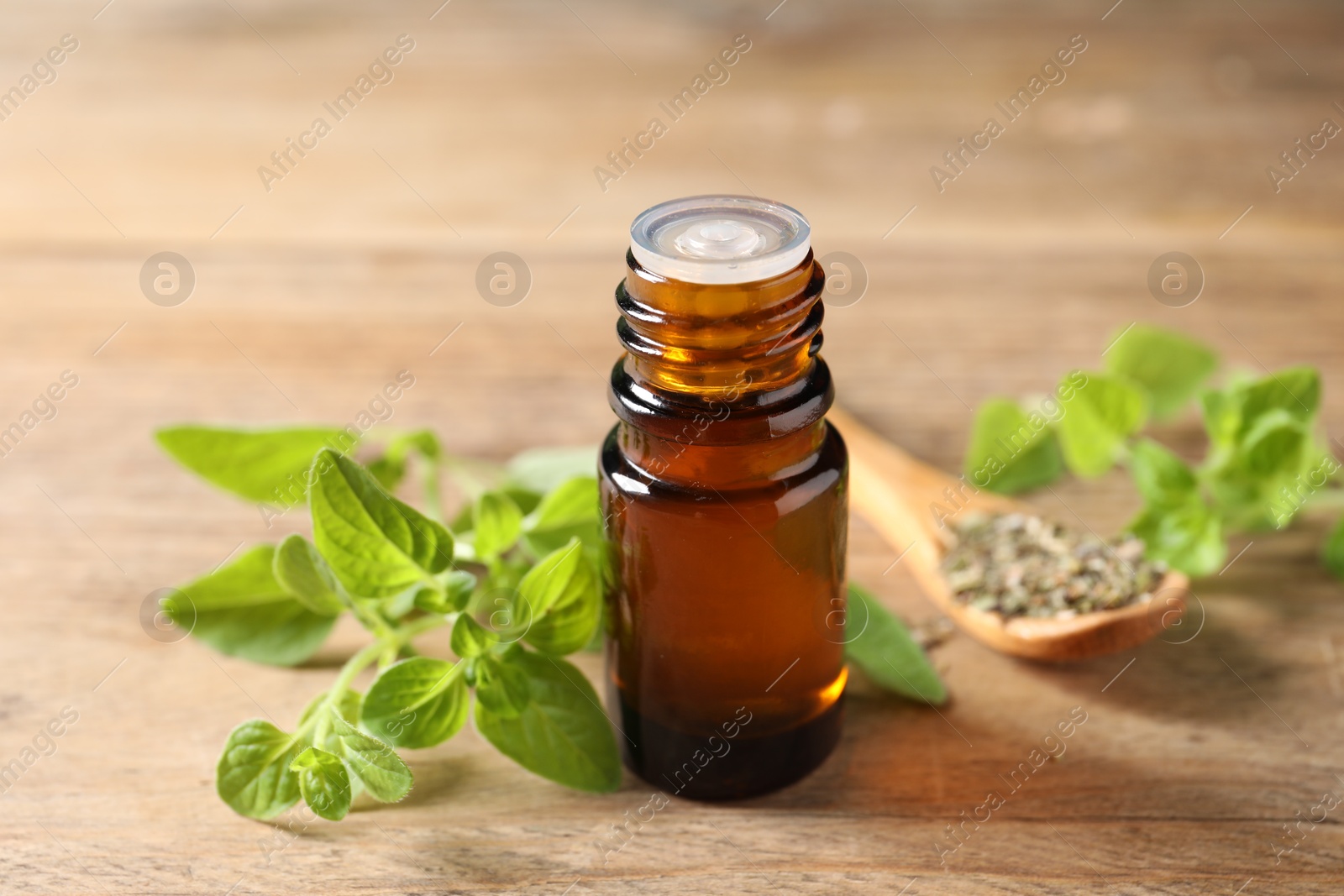 Photo of Essential oil in bottle and oregano twigs on wooden table, closeup