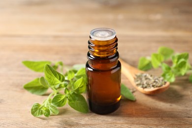 Photo of Essential oil in bottle and oregano twigs on wooden table, closeup