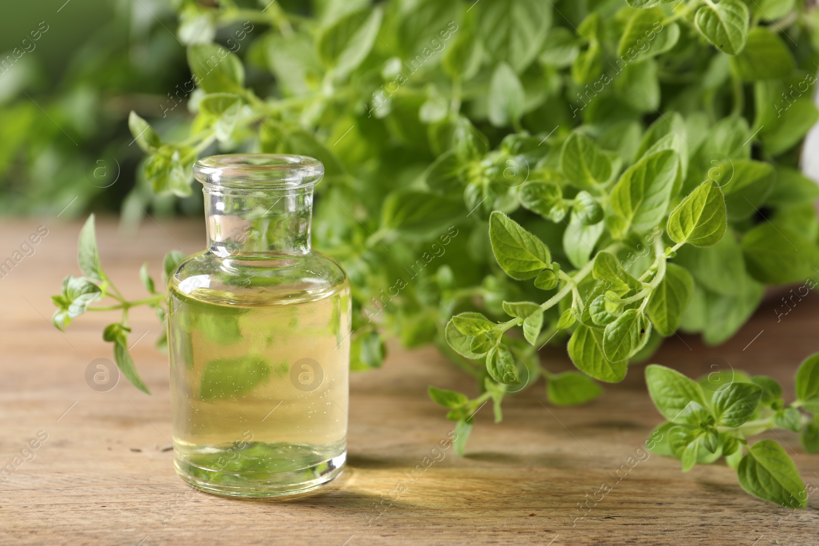 Photo of Essential oil in bottle and oregano twigs on wooden table, closeup