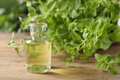 Essential oil in bottle and oregano twigs on wooden table, closeup