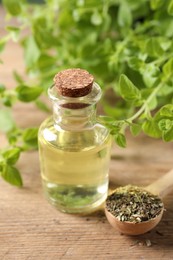 Essential oil in bottle, spoon with dry herb and oregano twigs on wooden table, closeup