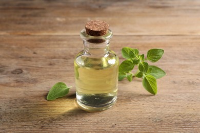 Photo of Essential oil in bottle and oregano leaves on wooden table, closeup