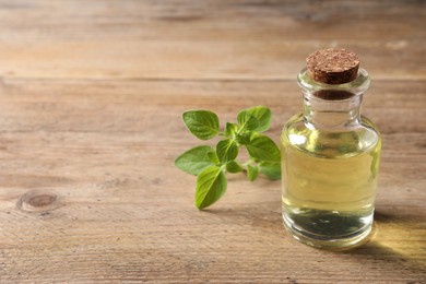 Photo of Essential oil in bottle and oregano twig on wooden table, closeup. Space for text