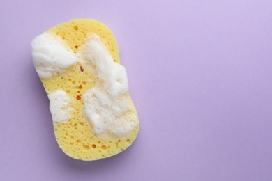 Photo of Yellow sponge with foam on violet background, top view