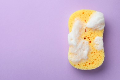 Photo of Yellow sponge with foam on violet background, top view. Space for text