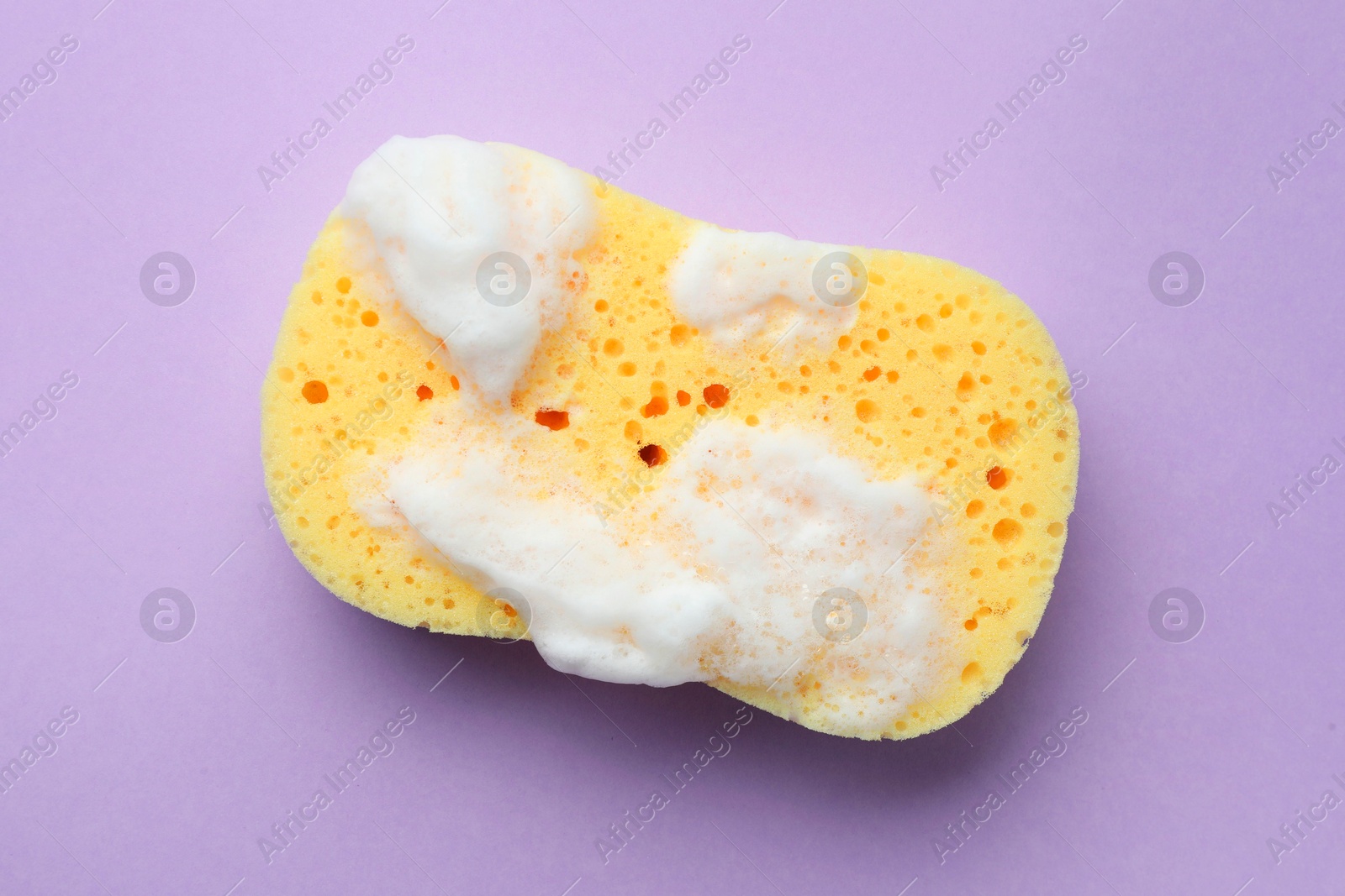 Photo of Yellow sponge with foam on violet background, top view