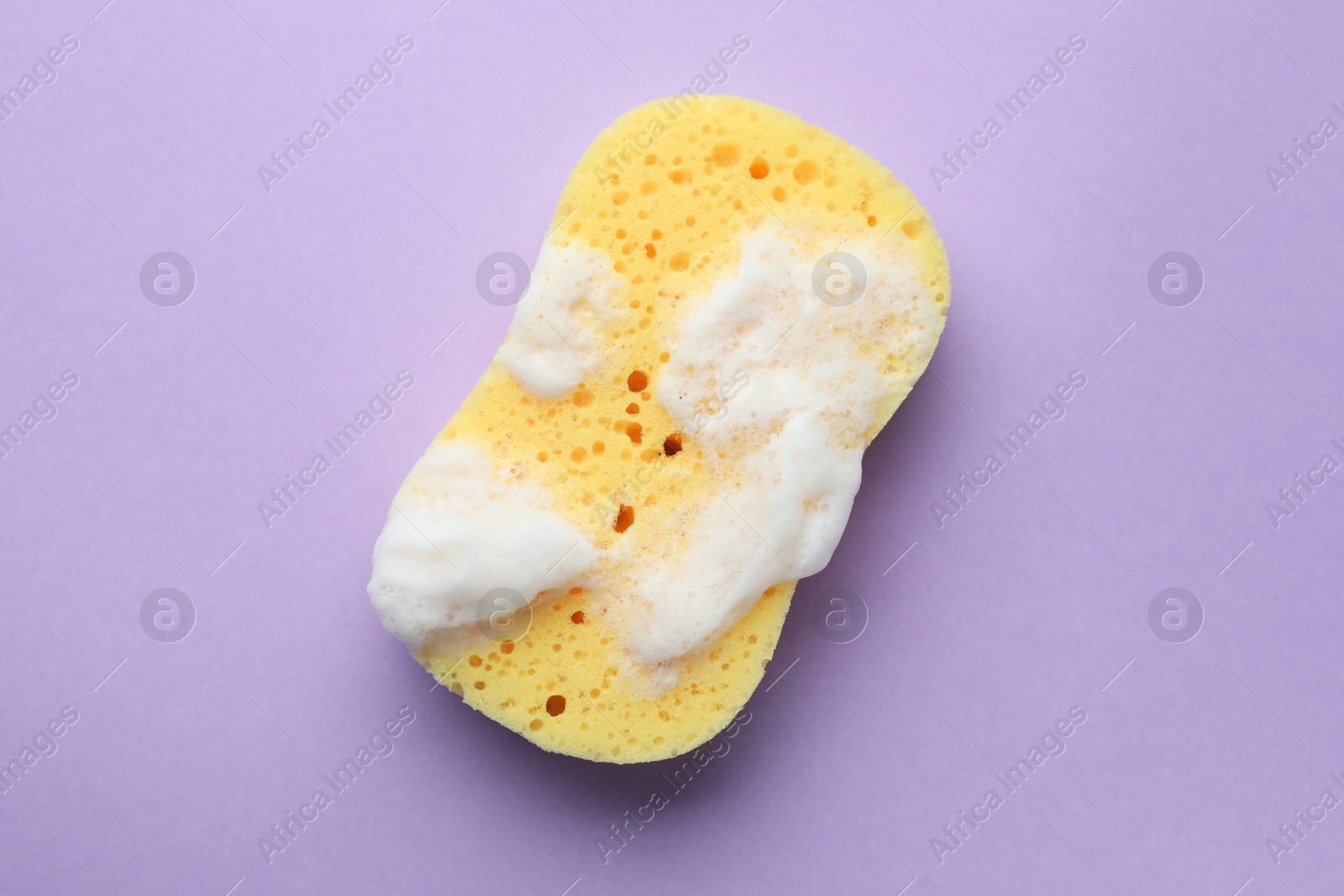 Photo of Yellow sponge with foam on violet background, top view