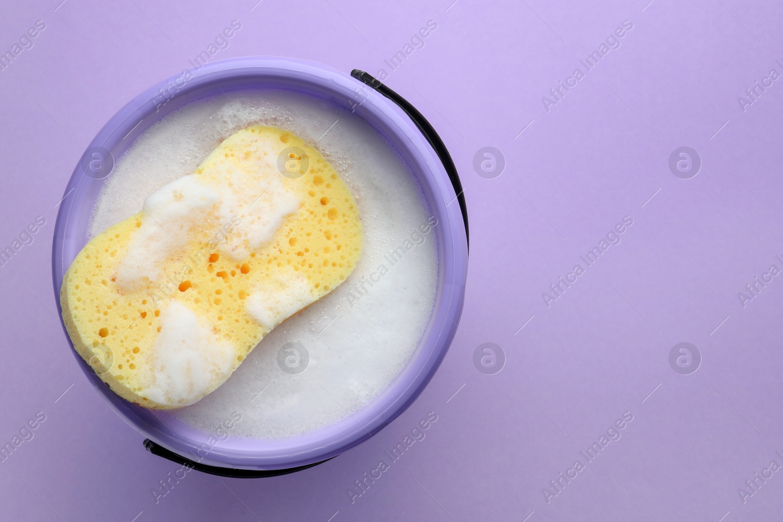 Photo of Bucket with foam and sponge on violet background, top view. Space for text