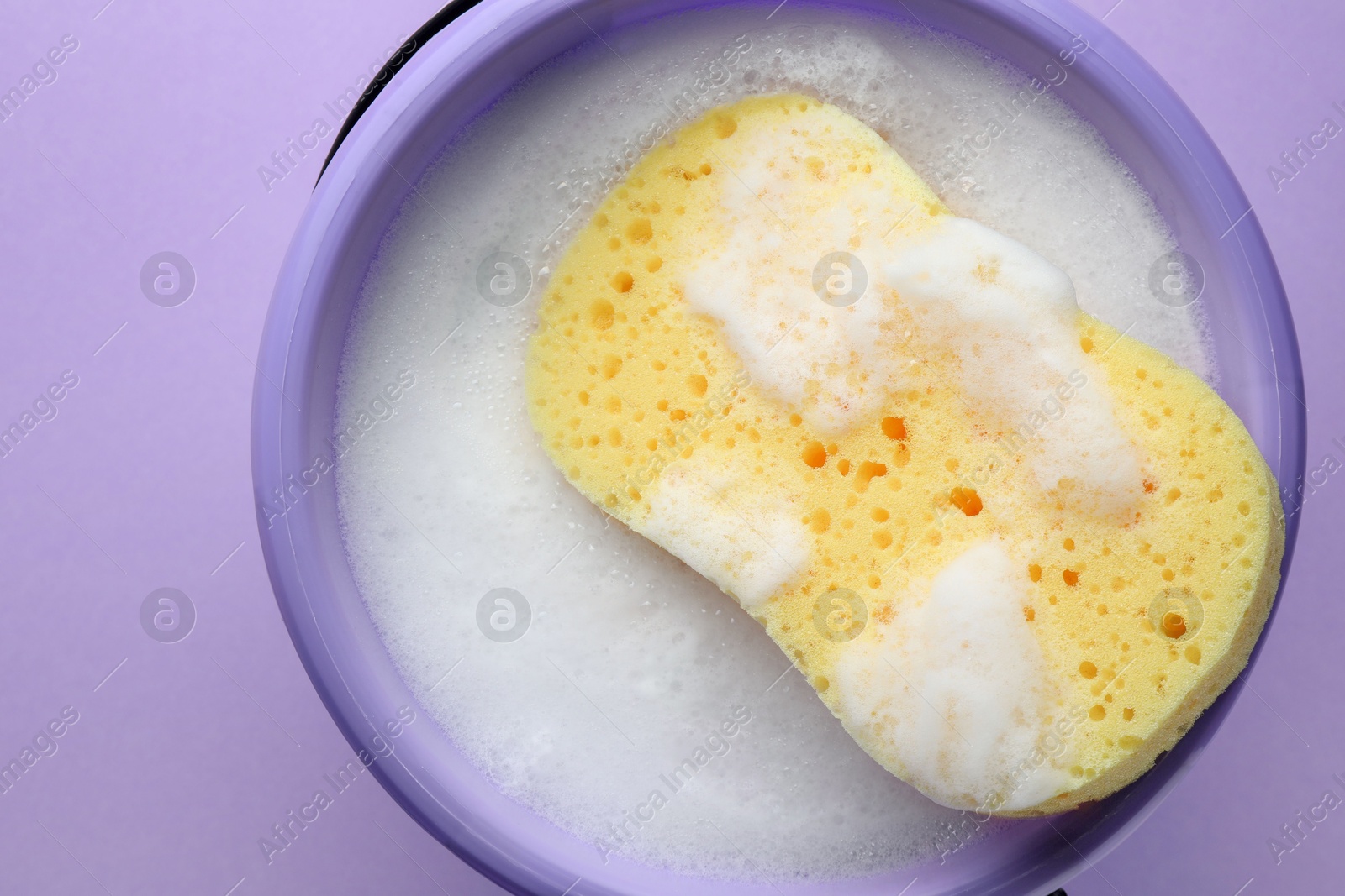 Photo of Bucket with foam and sponge on violet background, top view