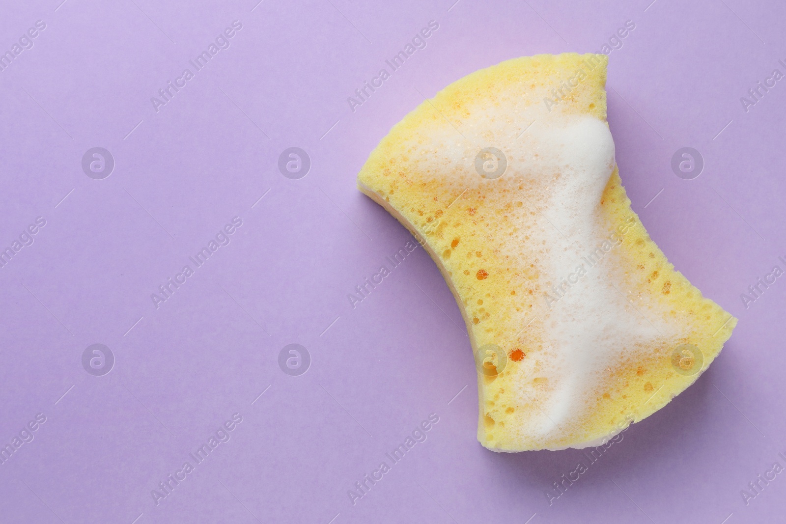 Photo of Yellow sponge with foam on violet background, top view. Space for text