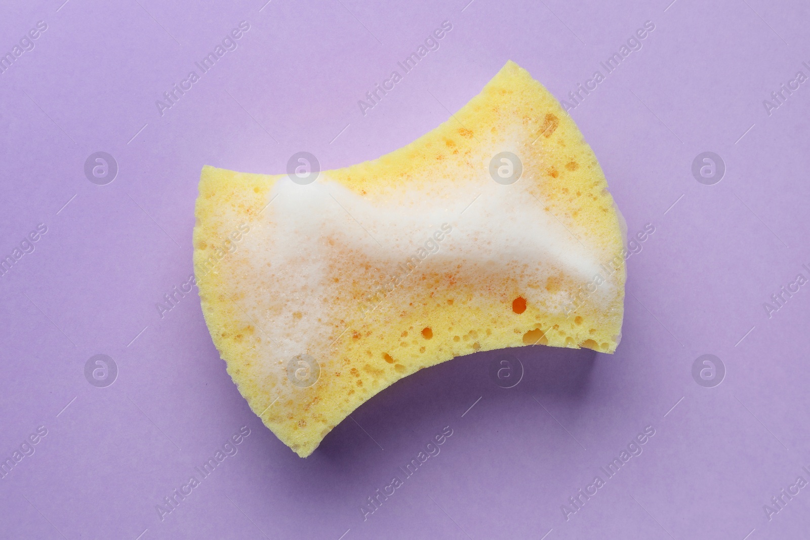 Photo of Yellow sponge with foam on violet background, top view