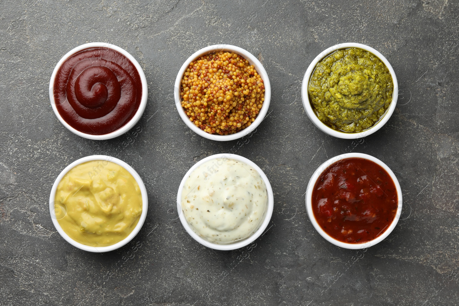 Photo of Many different sauces in bowls on grey table, top view