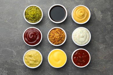 Photo of Many different sauces in bowls on grey table, top view