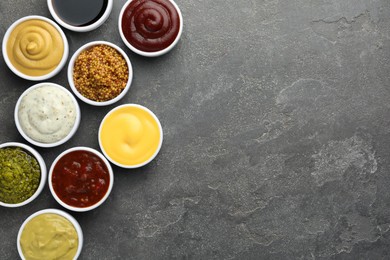 Photo of Many different sauces in bowls on grey table, top view. Space for text
