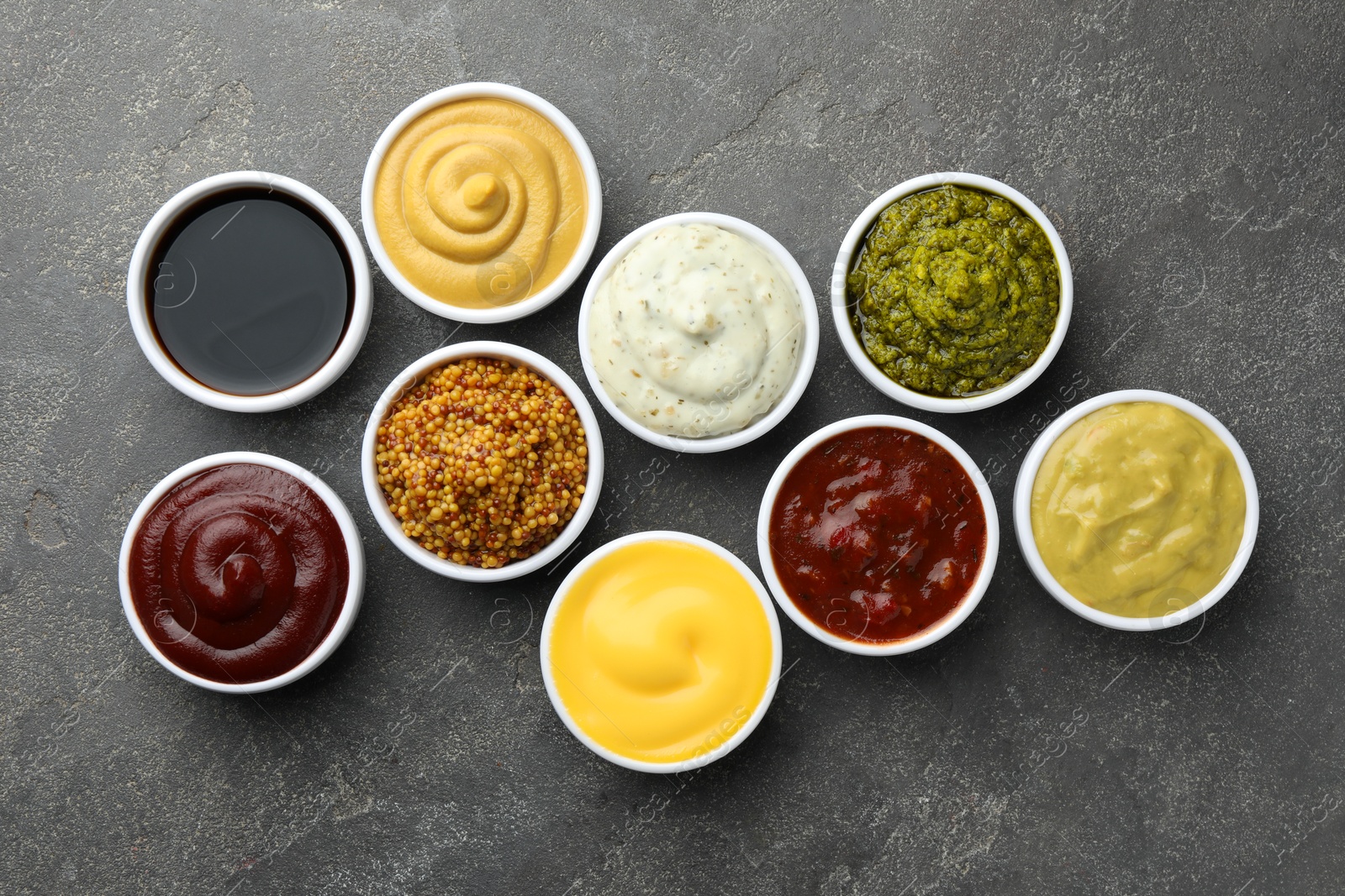 Photo of Many different sauces in bowls on grey table, top view