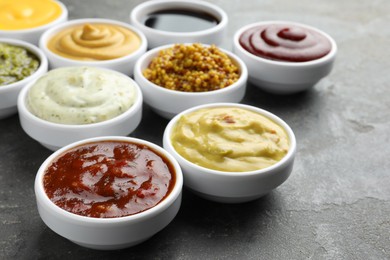 Photo of Many different sauces in bowls on grey table, closeup