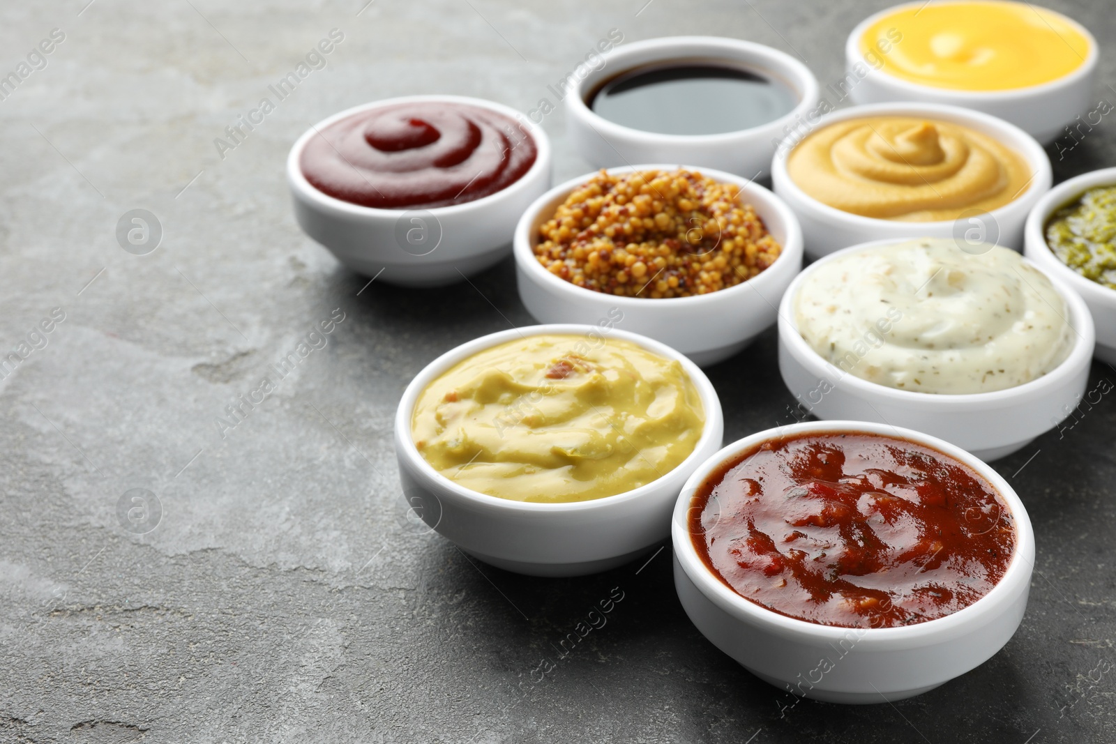 Photo of Many different sauces in bowls on grey table, closeup. Space for text