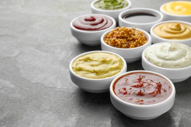 Photo of Many different sauces in bowls on grey table, closeup. Space for text