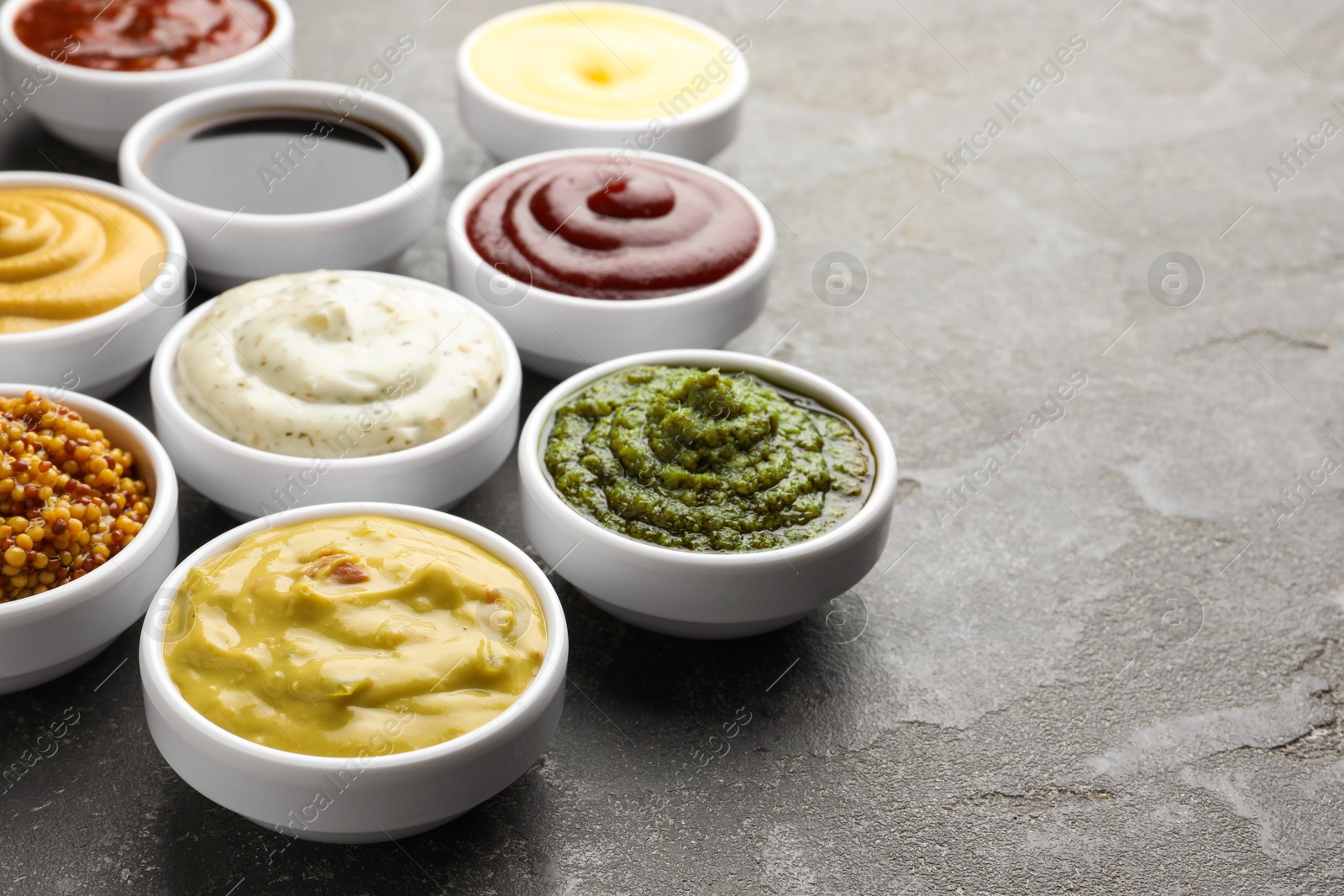 Photo of Many different sauces in bowls on grey table, closeup. Space for text