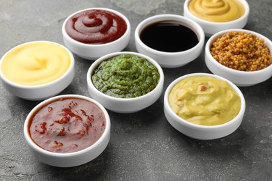 Photo of Many different sauces in bowls on grey table, top view