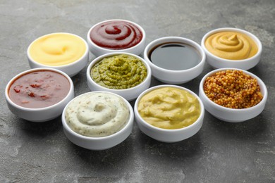 Photo of Many different sauces in bowls on grey table