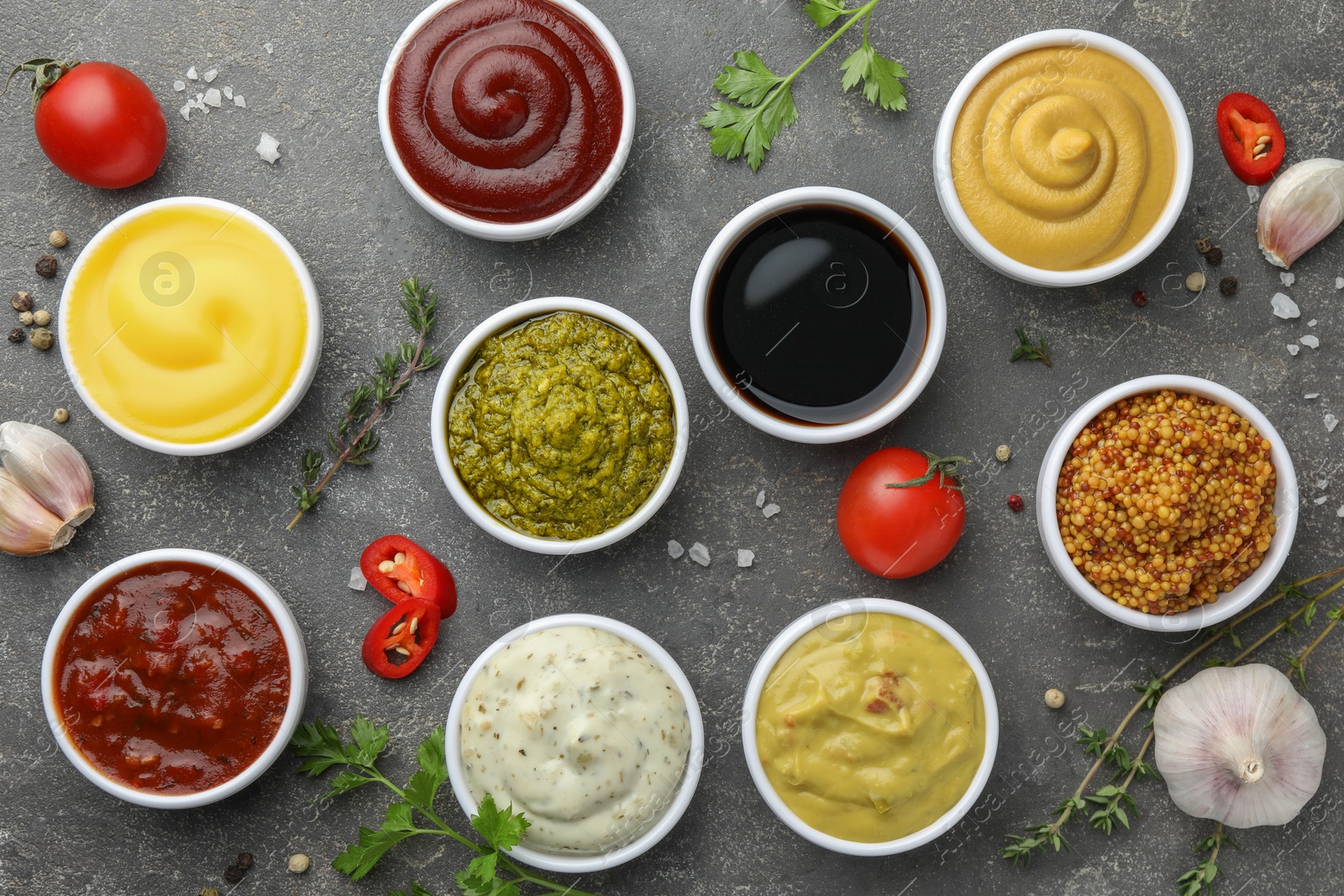 Photo of Many different sauces and spices on grey table, flat lay