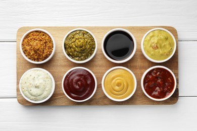 Photo of Many different sauces in bowls on white wooden table, top view