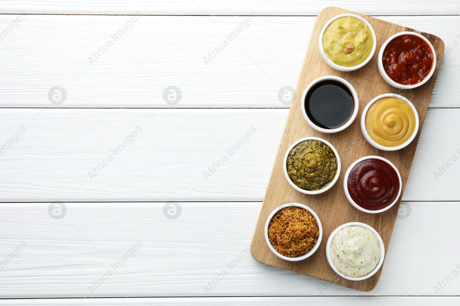 Photo of Many different sauces in bowls on white wooden table, top view. Space for text