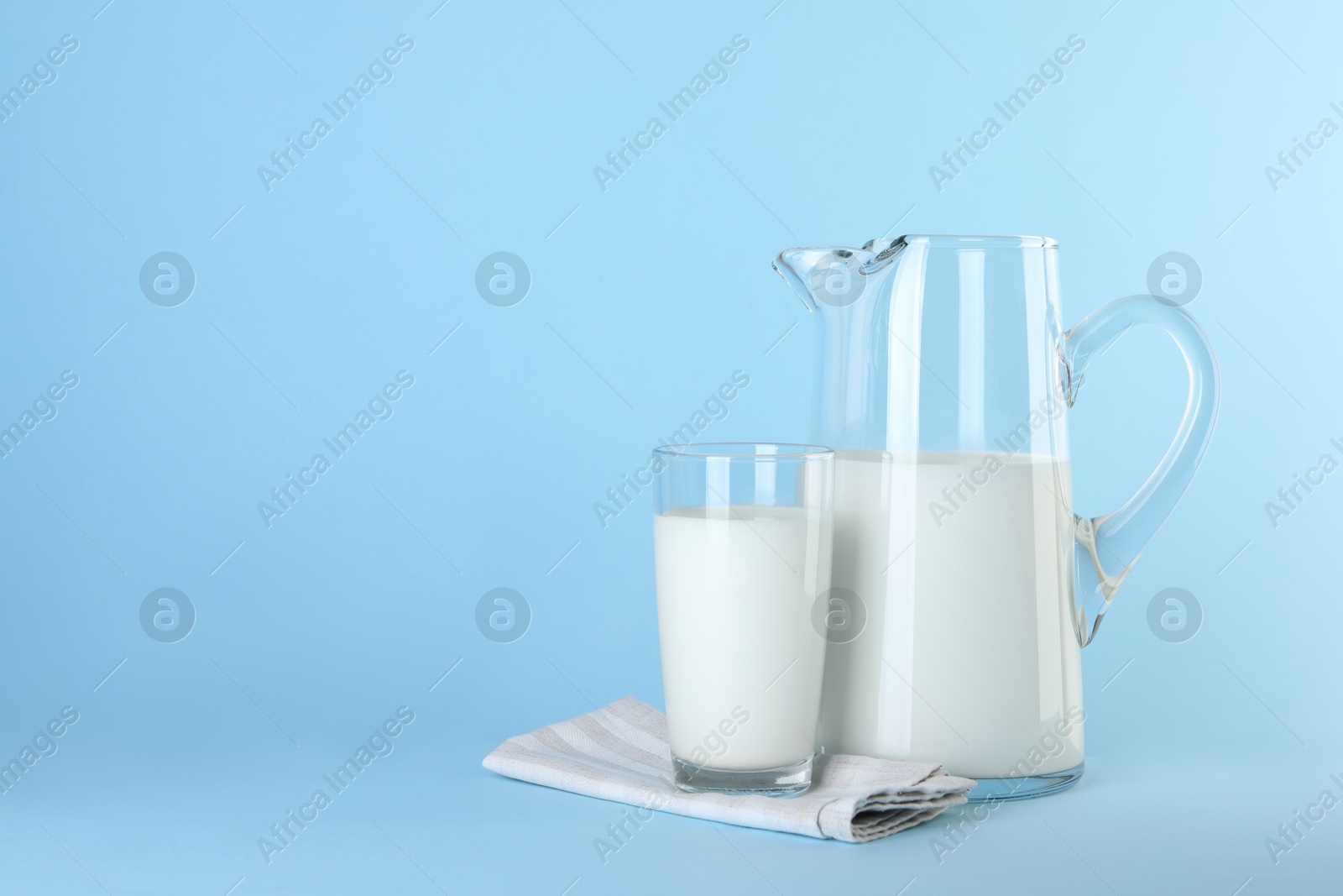 Photo of Jug and glass of fresh milk on light blue background, space for text