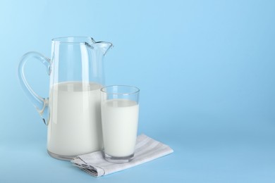Photo of Jug and glass of fresh milk on light blue background, space for text