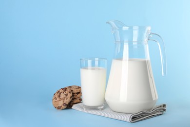Photo of Jug of fresh milk, glass and cookies on light blue background, space for text