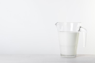 Photo of Jug of fresh milk on table against white background, space for text