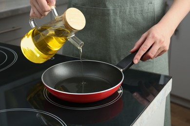 Photo of Vegetable fats. Woman pouring oil into frying pan on cooktop in kitchen, closeup