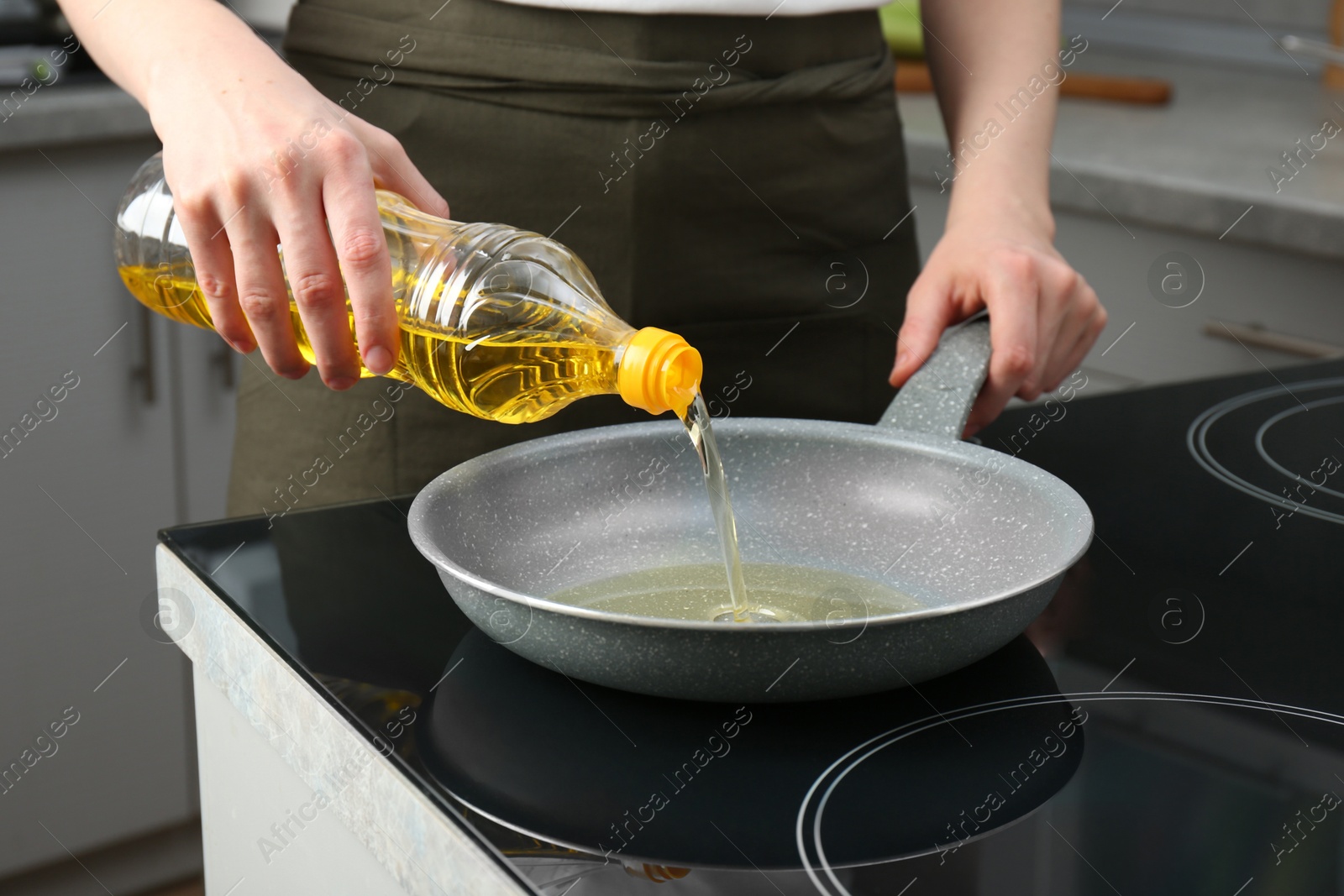 Photo of Vegetable fats. Woman pouring oil into frying pan on cooktop in kitchen, closeup