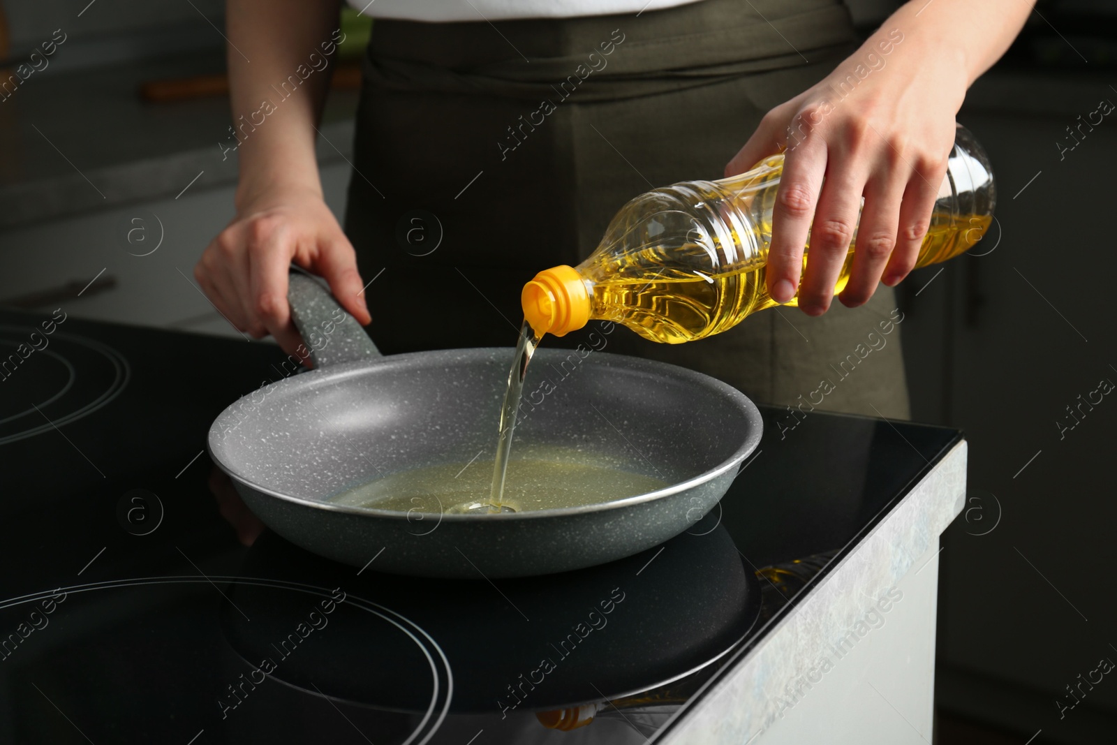 Photo of Vegetable fats. Woman pouring oil into frying pan on cooktop in kitchen, closeup